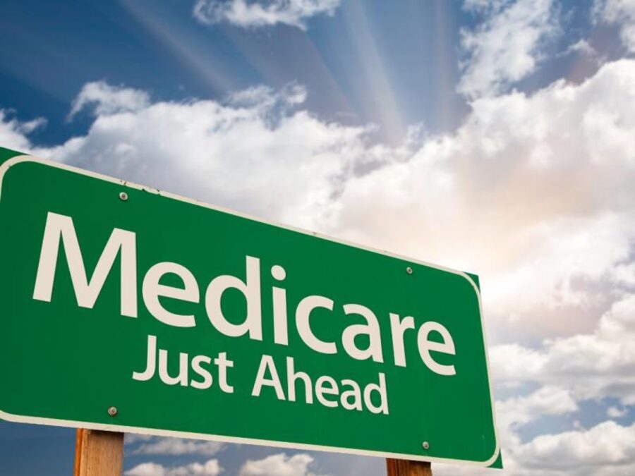 Green highway sign reading "Medicare Just Ahead" against a bright sky